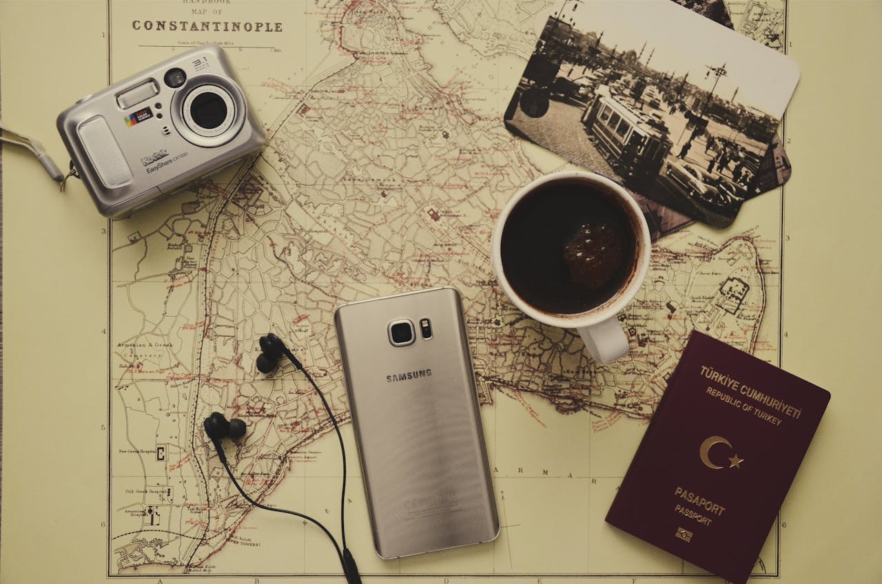 Flat lay of travel essentials including a map, passport, coffee, and gadgets on a desk.